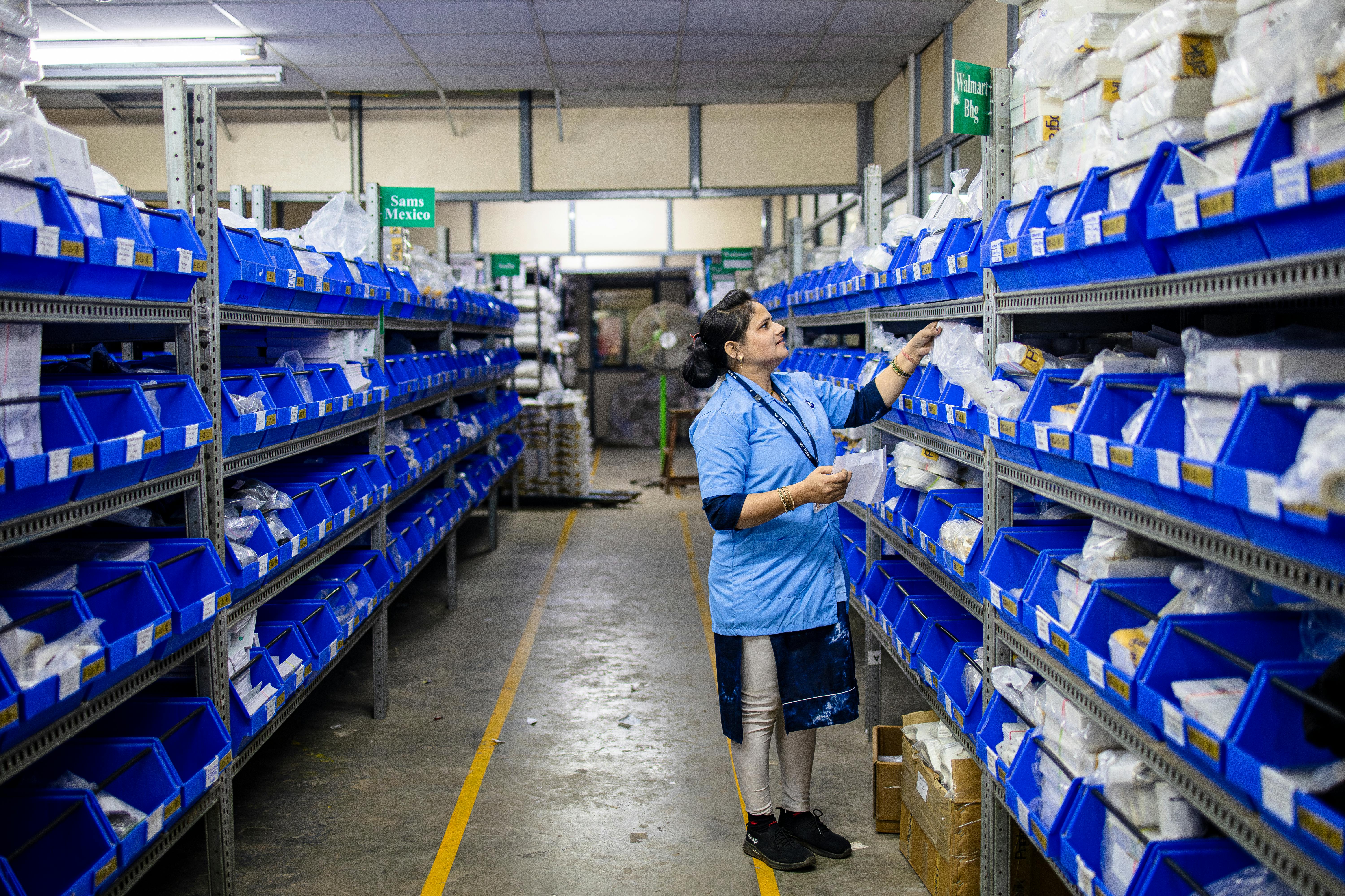 A worker in a warehouse organizing inventory on shelves with blue bins.